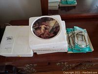 Four collectible cherub-themed plates stacked together, one visible with cherub image, dusty, in foam packaging.