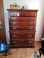 Front view of the wooden dresser showing five drawers with brass handles and carved detail on the top drawer