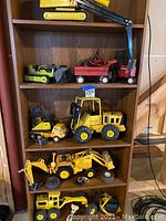 Four-shelf wooden bookcase displaying multiple metal toy vehicles and parts