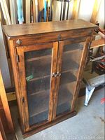 Front view of closed wooden cabinet with two textured glass doors and ring handles.