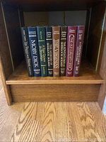 Books displayed on a wooden shelf showing full set standing upright.