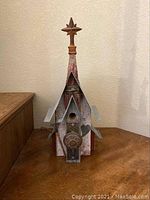 Front view of wooden birdhouse shaped like a church with star finial, large round door knob, metal peaked roof, and heart decoration.