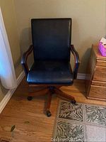 Front view of one chair showing black leather seat, back, wooden arms and swivel base