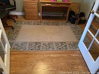 Full view of the rug placed on a hardwood floor in front of wooden office furniture and chairs.