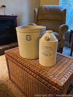 Photo showing a beige stoneware crock with a cobalt number 3 and a cream stoneware batter jug stamped by The Western Pottery Co Denver on a woven chest in living room.