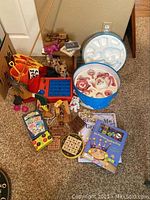 Overall assortment of toys and games including vintage tea set, wooden animal figurines, games, and books arranged on carpet.