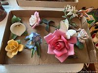 Top-down photo of seven Lenox porcelain flower figurines in a box with various colors including pink, yellow, blue, and white.