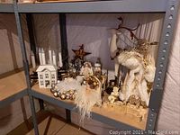 Shelf displaying all Christmas decor items including white house window candle, Santa figurine, angel figurine, and Believe sign with candle holders