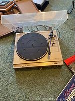 Gold-colored vintage turntable record player with tonearm and speed switch, set on green carpet.