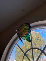 Side view of stained glass butterfly hanging in front of arched window showing yellow, green and blue wings and black antennae with beads.