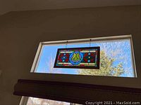Stained glass panel hung in dining room transom window, showing central circular motif and surrounding geometric pattern.
