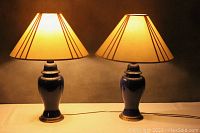 Pair of cobalt blue ceramic lamps with white shades lit up on a table.