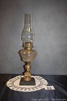 Full view of the antique kerosene oil lamp with figural stem and chimney standing on a lace doily.