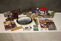 Full lot overview showing all railroad items including wooden trains, clock, cast iron door stops, ceramic cookie jar, pencil box, figurines, catalogs, and game case.