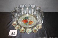 Serving tray with floral design surrounded by six floral coasters and eight clear ribbed glasses, black background
