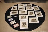 Top-down photo showing all 17 unframed matted black and white prints arranged in neat rows on a black cloth surface. Shows the overall layout and number of prints.