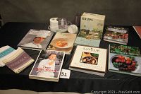Full view of all cookbooks, tea towels, food processor, and can opener arranged on a black surface