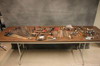 Overview showing a large selection of hand tools spread out on a table including saws, files, screwdrivers, braces, and other hand tools.
