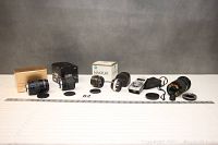 Full lineup of lenses and accessories placed in a row on a white surface with a measurement ruler in front.