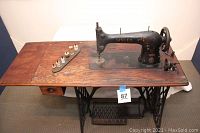 Full view of the antique Singer treadle sewing machine with wooden top and cast iron base, showing the overall condition and included accessories such as thread spools.