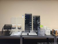 Overview of assorted file organizers including black tiered magazine holders on left, clear acrylic dividers and organizers in middle, white metal shelves and wall grids on right