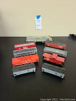 Photo of 9 HO gauge train cars including a gray and yellow L&N engine and various freight cars with different railroad markings and color schemes on a black surface.