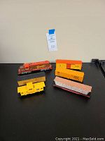 Overview of all 5 model train cars including Burlington locomotive, Union Pacific caboose, Dow Chemical and DowAgroSciences freight cars, and a flatbed car with logs.
