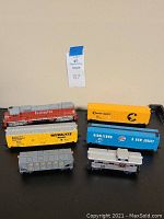 Six HO gauge model trains arranged on a black surface, showing various brands and colors including Burlington, Milwaukee Road, Chessie System, Monon, and Middletown & New Jersey.