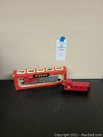 Photo showing the locomotive in box next to the red caboose on black surface with beige background.