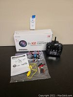Photo of LH-X2 quadcopter drone, remote control, USB charger, battery clips, user manual, and product box with camera lens graphic.
