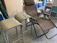 Full view of reclining lounge chair next to two matching bar stools with grey metal frames and mesh seats.