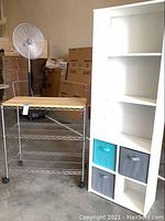 White tall shelf unit with four fabric storage cubes and chrome metal shelf with wooden top on casters shown together.