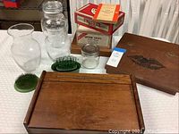 Photo showing wooden boxes including a large one with an eagle carved lid, clear glass jars and textured vases, and green metal flower frogs.