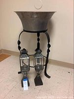 Full view of the metal planter with wrought iron stand and the two candle holders on floor.