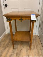 Full frontal view of oak side table with decorative metal accents and lower shelf