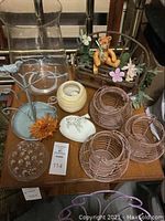 Photo of small decor items on wood table including candleholder, toy bench, metal stand, lanterns, zebra ring dish, flower frog, and glass pieces.