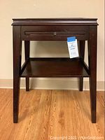 Front view of small dark wood writing table showing drawer and lower shelf.