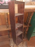Vertical wooden shelving unit, stained plywood with two shelves, shows wear and dust