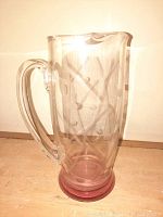 Photo of pink Depression glass pitcher standing on surface showing etched geometric and dot pattern with handle and flared lip.