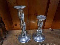 Two cast aluminum twisted candle sticks, one 12 inches and the other 9 inches tall, placed against a wooden background for size and design visibility.