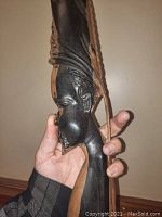 Side view showing the tall elongated head with detailed facial features and blond and black swirl ebony wood grains. Hanging cord attached.