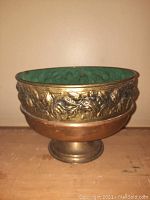 Front angle of oval copper and brass planter pot showing embossed floral design and green patina interior