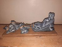 Side view of entire dog sled team with four dogs and sledder on sled mounted on oak base