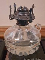 Clear glass antique oil lamp with silver plated burner showing finger loop and scalloped base design.