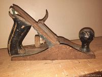 Front angle view of hand plane showing black rear handle with chipped paint and rust on metal body.