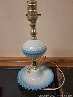 Lamp full view showing hobnail plastic design in white and blue gradient with brass neck and socket.