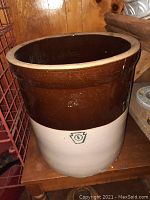 Photo of large two-tone stoneware crock showing brown upper half and beige lower half with '6' emblem on front, placed on wooden table.