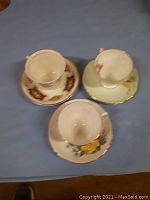 Three bone china teacups with matching saucers arranged on a blue surface, each decorated with different floral patterns.