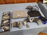 PlayStation 1 and PlayStation 2 consoles on a blue surface showing controllers and cables