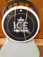 Round Labatt Ice Beer light-up sign displaying front, sitting on chair, cord wrapped around face.